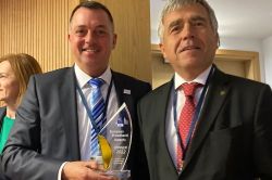 2 männliche Personen, die linke Person hält die Auszeichnung "EU-Breitband-Oscar" in der Hand.